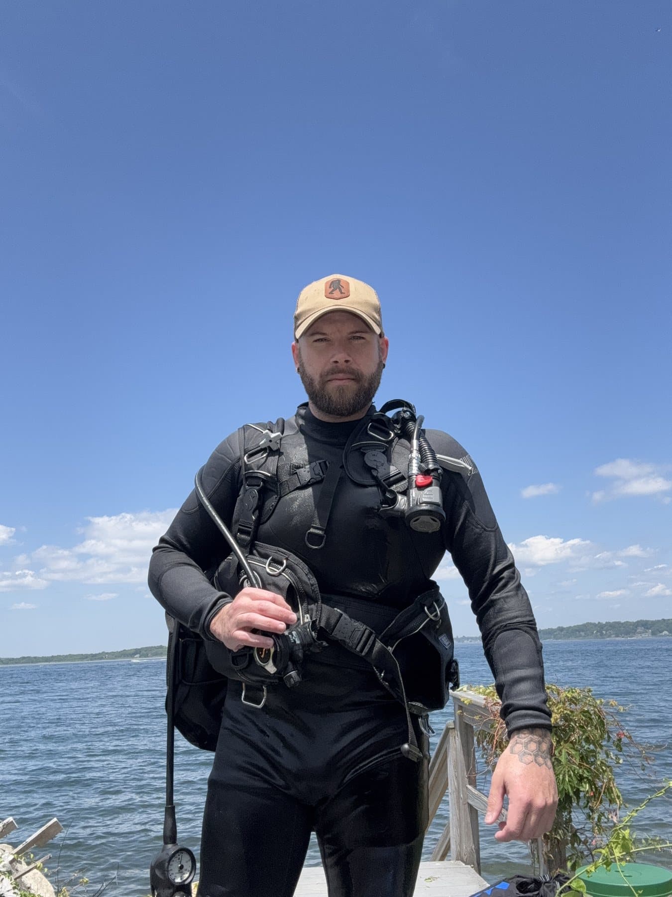 Diver standing on shore in drysuit with water behind