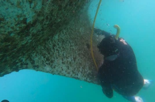 Diver cleaning along a boat hull underwater