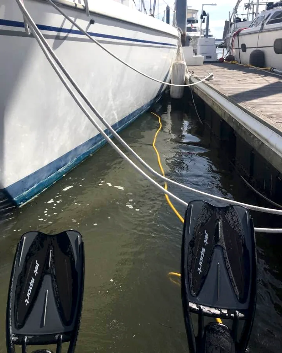 Dive fins and service hose beside a sailboat in a marina slip